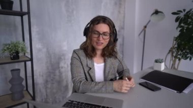 Video görüşmesi sırasında bilgisayar kullanan kulaklıklı güzel bir iş kadını. Uzaktan çalışma konsepti. Görevdeki genç bayan.