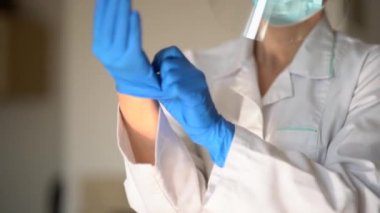Tıbbi maskeli genç bir kadın terapist koluna koruyucu steril eldiven takar, koronovirüse karşı korur. Lastik eldivenli doktor, konsept sterilite saflık, tıbbi klinik