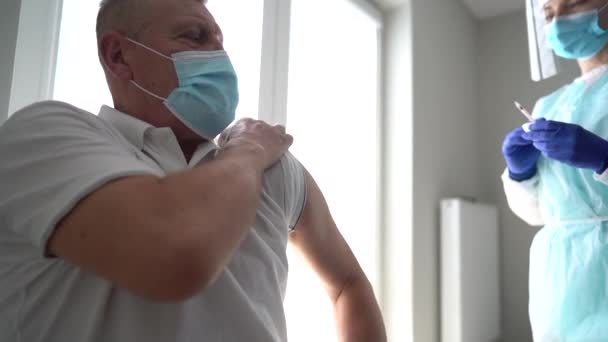 Verpleegster die per spuit het vaccin tegen COVID-19 op de deltaspier aanbrengt bij een oudere man met masker in het kantoor van de arts. Gezondheidsbescherming, vaccinatie en gezondheidszorg — Stockvideo