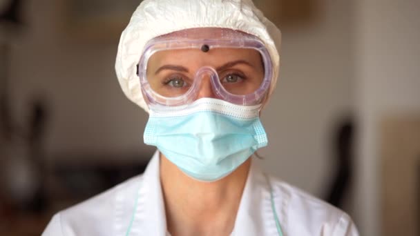 Närbild porträtt av en svälttrött läkare i en skyddande mask med glasögon och en mössa. Infektionist under koronavirusepidemin COVID-19 — Stockvideo