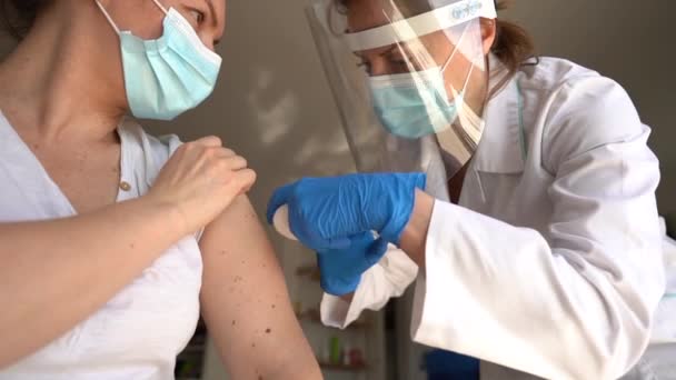 Nahaufnahme eines Arztes in steriler Schutzkleidung, der einer jungen Frau mit besorgtem Gesichtsausdruck einen Covid-19-Impfstoff in die Schulter spritzt. Impfzeit. Globale Pandemie — Stockvideo