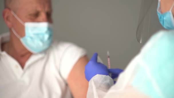 Ein älterer Mann kaukasischen Aussehens mit Maske erhält zu Hause eine Dosis Coronavirus-Impfung, der Arzt kommt zum Patienten, um ihm eine Schutzspritze gegen die Krankheit zu geben — Stockvideo