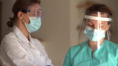 Koruyucu maskeli iki kadın doktorun portresi. Bir hastaya reçete yazmadan önce iki meslektaş danışmanlık yapıyor. Hastanede iki hemşire.
