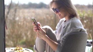 Güneş gözlüğü takan sevimli yetişkin kadın piknik sırasında akıllı telefonunu kullanıyor. Güneşli hava, iyi tatiller.