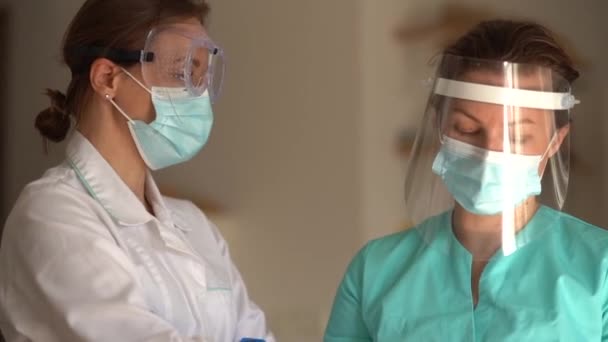 Retrato de dos doctores con máscaras protectoras. Dos colegas consultan antes de prescribir tratamiento para un paciente. Dos enfermeras en un hospital — Vídeos de Stock