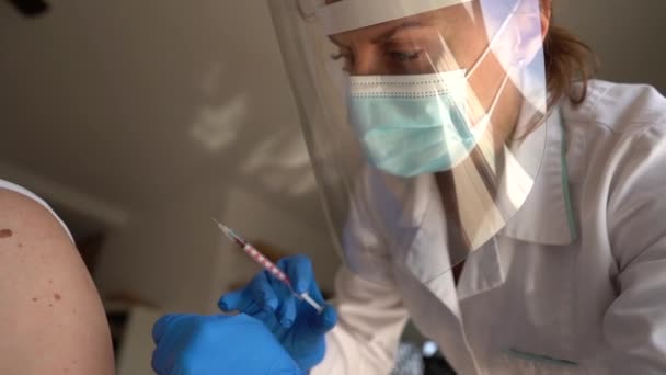 Primer plano de una doctora en una máscara protectora y escudo hace una inyección de la vacuna contra el coronavirus covid-19. Concepto de vacunación — Vídeos de Stock