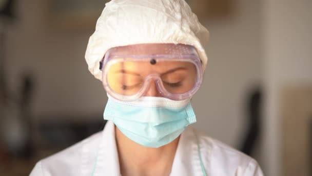 Уставший доктор, близкий портрет. Женщина-врач в защитной маске, очках и кепке. Доктор во время пандемии коронавируса — стоковое видео