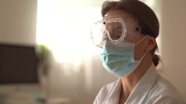 Лицо уставшего врача в защитной хирургической маске и очках. Пандемия коронавируса ковид-19, женщина-терапевт — стоковое видео