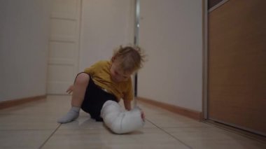 Tatlı çocuk, bacağındaki kazara kırıktan sonra alçıyla dairede dolaşıyor. Evde kırık bir bacağın iyileşmesi, sağlık sigortası konsepti. 4K