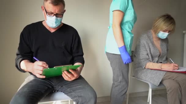 Vaccinatie van risicogroepen tegen coronavirusinfectie. Een man en een vrouw die met pensioen gingen in een ziekenhuis vullen papieren in voordat ze worden gevaccineerd tegen covid-19. Immunisatieprocedure — Stockvideo