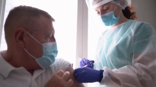 Starszy mężczyzna otrzymuje szczepionkę przeciw koronawirusowi. Przyjazna pielęgniarka szczepiąca starszego pacjenta przeciwko grypie, grypie, zapaleniu płuc lub koronawirusowi — Wideo stockowe