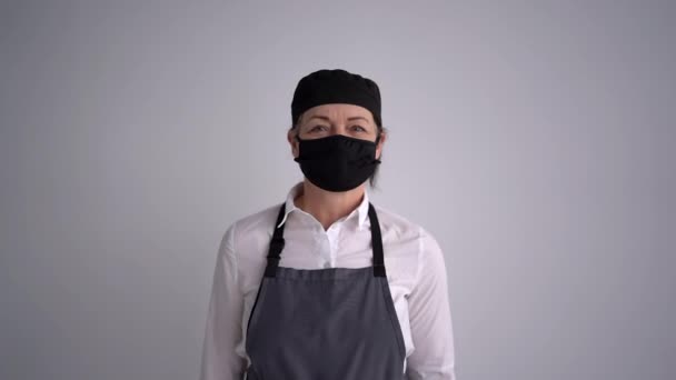 Cozinheiro ou chef de pastelaria, inicialização durante uma pandemia. Retrato de uma cozinheira feminina em uniforme e em uma máscara protetora e luvas em preto. Uma mulher segurando um rolo de madeira. Nova realidade — Vídeo de Stock