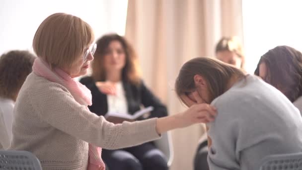 Jonge vrouw deelt haar verhaal en huilt tijdens een groepsontmoeting met een psychotherapeut. Een volwassen vrouw steunt haar. Groepstherapie. Psychologische hulp — Stockvideo