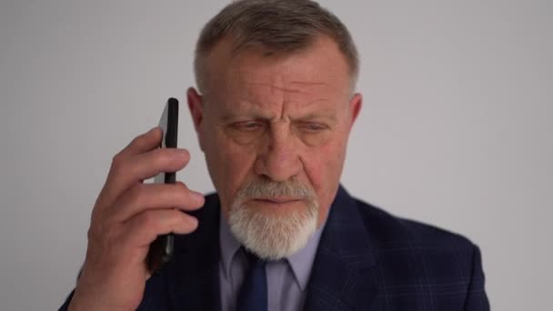 成熟した成功したビジネスマンの近い肖像画。電話で話しているビジネススーツの深刻な灰色の髭の男 — ストック動画