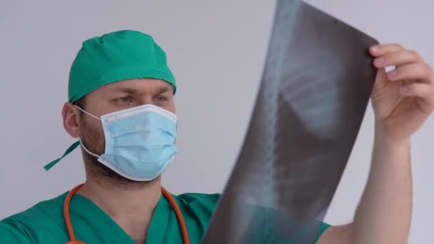 Medico maschio in maschera e mantello verde contenente raggi X o roentgen dei polmoni, fluorografia. Diagnosticare danni polmonari durante la pandemia di coronavirus covid-19 — Video Stock