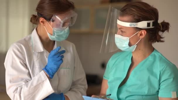 検査結果や治療の経過を議論する病院の廊下で会う女性医師,コロナウイルスパンデミックの間に外科的フェイスマスクを着用 — ストック動画