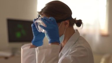 Yan görüş. Yorgun kadın doktor gözlüğünü ve maskesini çıkarıyor. Salgın Coronavirus covid-19 sırasında doktorda çalışma gününün sonu.