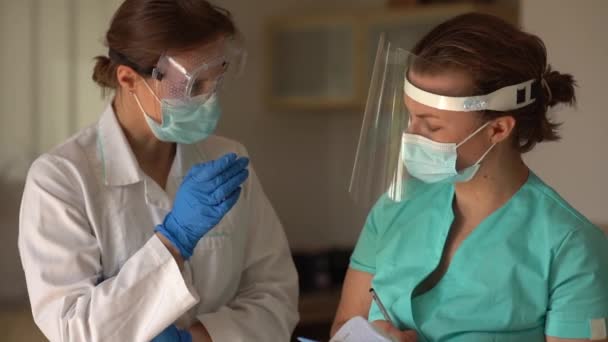 Zwei Ärztinnen oder ein Arzt und eine Krankenschwester mit Schutzmasken und Handschuhen diskutieren die Diagnose und Behandlung der Patientin. Kollegen beraten sich — Stockvideo
