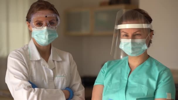 의사 2 명의 초상화가 카메라를 자세히 들여다보고 있습니다. 코로나 바이러스가 유행하는 동안 의사들은 직업을 가졌다. 두 명의 여성 의사 동료 — 비디오