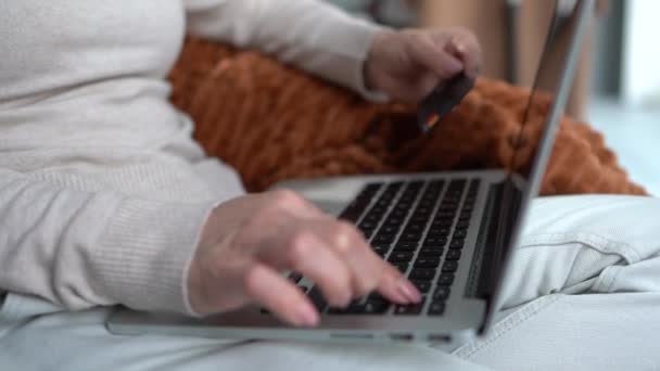 Chiuda il ritratto di una mano di donne che tiene una carta di banca ed entra in un numero sulla tastiera di computer portatile. Shopping online e e-commerce concetto. Donna ordina generi alimentari durante una pandemia — Video Stock