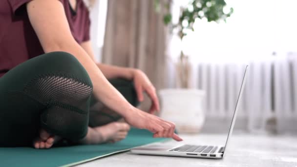 Online-Schulungen zu Hause. Schlanke Frau praktiziert Yoga am Laptop und schaut Videos im Sitzen in Lotus-Position — Stockvideo