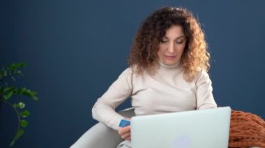 İnternetten alışveriş. Çekici kıvırcık saçlı kız dizüstü bilgisayar ve kredi kartı kullanarak alışveriş yapıyor. Evde kal konsepti