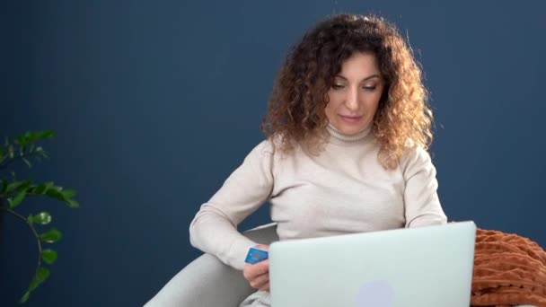 İnternetten alışveriş. Çekici kıvırcık saçlı kız dizüstü bilgisayar ve kredi kartı kullanarak alışveriş yapıyor. Evde kal konsepti — Stok video