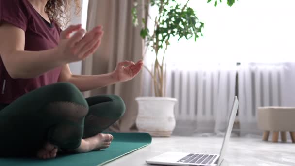 Çekici bir kız bir dizi ogi egzersizini dizüstü bilgisayarın yanında yoğurdun üzerinde otururken tamamlıyor. İnternetten yoga dersi. 4K — Stok video