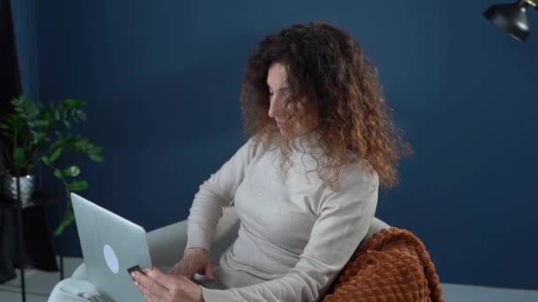 Çevrimiçi bankacılık kavramı. Yetişkin bir kadın evdeki faturaları dizüstü bilgisayar ve banka kartıyla ödüyor. Evde kal ve e-ticaret yap. — Stok video
