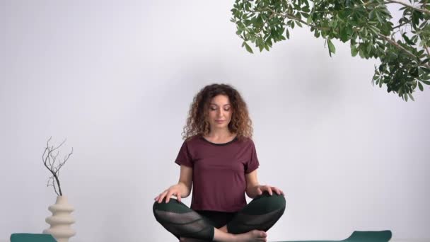 Die attraktive Lockenkönigin sitzt in der Lotusposition auf einer Yogamatte. Gesunder Lebensstil und Achtsamkeit — Stockvideo
