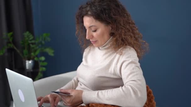 Portrait of a beautiful curly woman with a laptop and a credit card in her hands. The girl is shopping online. Online shopping from home, stay home — ストック動画