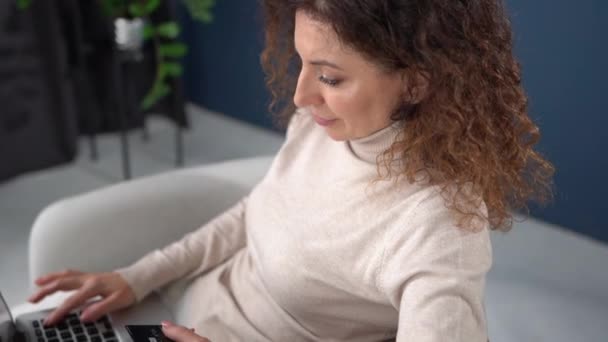 Close up portrait of a beautiful curly woman with a laptop and a credit card in her hands. The girl is shopping online. Online shopping from home, stay home — Vídeo de stock