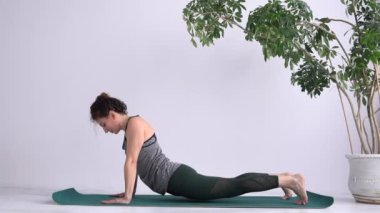 Attractive adult girl performs exercises while standing barefoot on a mat. Yoga Assana training. Exercises to stretch and strengthen your back muscles