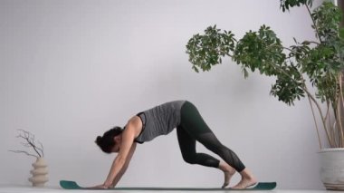 Yoga studio and instructor conducts a lesson. Attractive curly-haired girl practices classical yoga assanas while standing on the mat at home