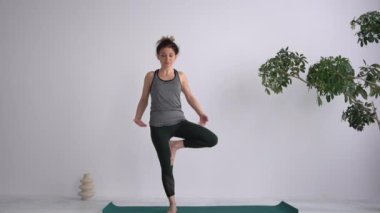 Yoga asana standing. Balance exercises. Attractive adult girl performs exercises while standing barefoot on the mat