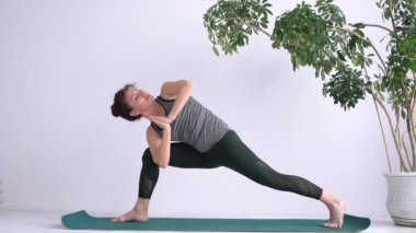 Side Angle or Side Lunge yoga position. Attractive adult girl performs exercises while standing barefoot on the mat