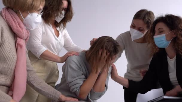 Woman in a mask talks and cries about a traumatic childhood experience during group therapy with a psychologist. Masked people in the psychologists office comfort a woman — Stockvideo
