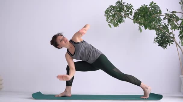 Zijhoek of Side Lunge yoga positie. Mooie vrouw oefent klassieke yoga asana terwijl ze thuis op de mat staat. Yoga lessen online en met een yoga studio — Stockvideo