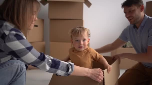 Retrato de marido e mulher brincando com seu filho em uma nova casa. Hipoteca, pessoas, habitação e conceito imobiliário. Família feliz se diverte em um novo apartamento — Vídeo de Stock