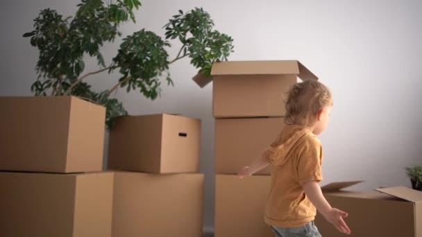Bebê bonito criança carrega uma caixa de papelão. A criança ajuda seus pais ao se mudar para uma nova casa. Conceito imobiliário — Vídeo de Stock