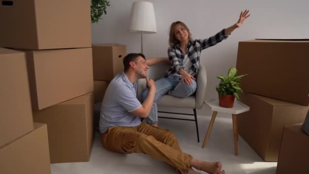 Mann und Frau planen, ihre Habseligkeiten aus den Kartons in ihrem neuen Zuhause auszupacken. Umzugs- und Immobilienkonzept, glückliche Familie — Stockvideo