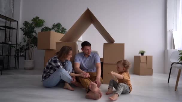 Famiglia felice con un bambino che gioca in una nuova casa. Padre, madre e figlio si divertono insieme. Trasloco giorno casa e concetto immobiliare — Video Stock