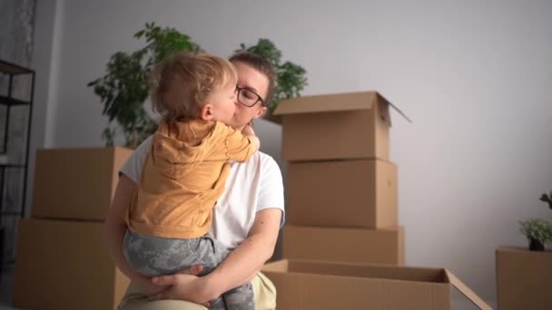 Mãe e filho, mãe com criança nos braços contra o fundo de caixas de papelão, realocação e mudança para um novo apartamento — Vídeo de Stock