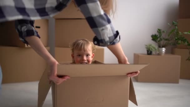 Mladá matka si hraje s dítětem, které sedí v lepenkové krabici. Rodina se stěhuje do nového bytu, máma a syn mají fanouška během stěhování — Stock video
