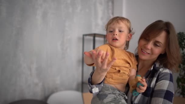 Olgun bir annenin portresi, kollarında yürümeye başlayan bir bebekle karton kutuların arka planında. Parmaklar sayılıyor. Anneler Günü — Stok video