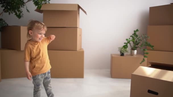 Das blonde Kind tanzt auf dem Hintergrund von Pappkartons. Umzug, Immobilien und neues Wohnungskonzept — Stockvideo