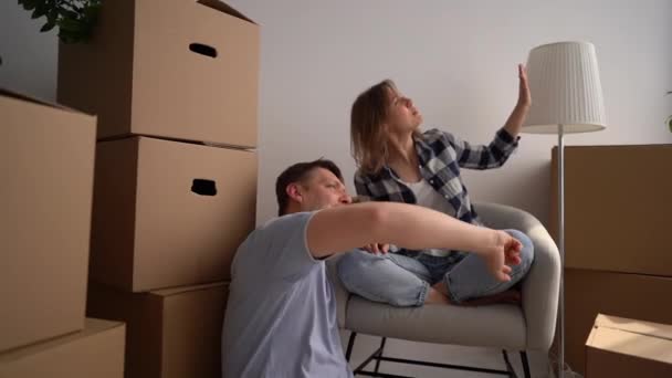 Marido e esposa sentar entre caixas de papelão. Happy young family discute um plano para uma nova casa imediatamente após a realocação — Vídeo de Stock