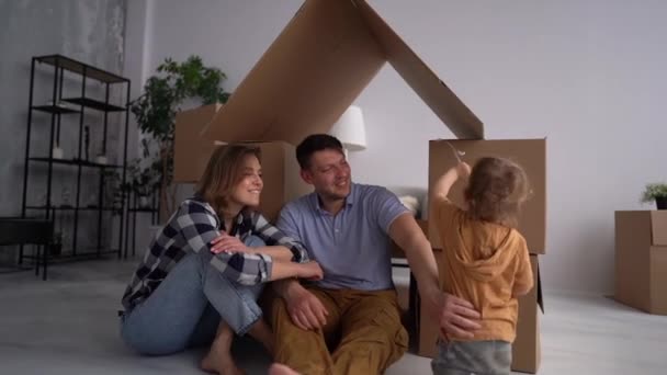 Een portret van een jong gezin met een peuter die in een nieuw huis intrekt. Vader, moeder en kind hebben plezier samen. Verhuisdag en vastgoedconcept — Stockvideo