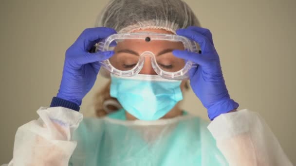 美しい女性医師は、作業日の開始前に彼女の顔に保護マスクを調整します。コロナウイルス｜covid-19 — ストック動画