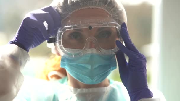 Médica com roupa protetora, máscara e óculos durante a quarentena covid-19. Enfermeira do hospital ajustando óculos de segurança — Vídeo de Stock